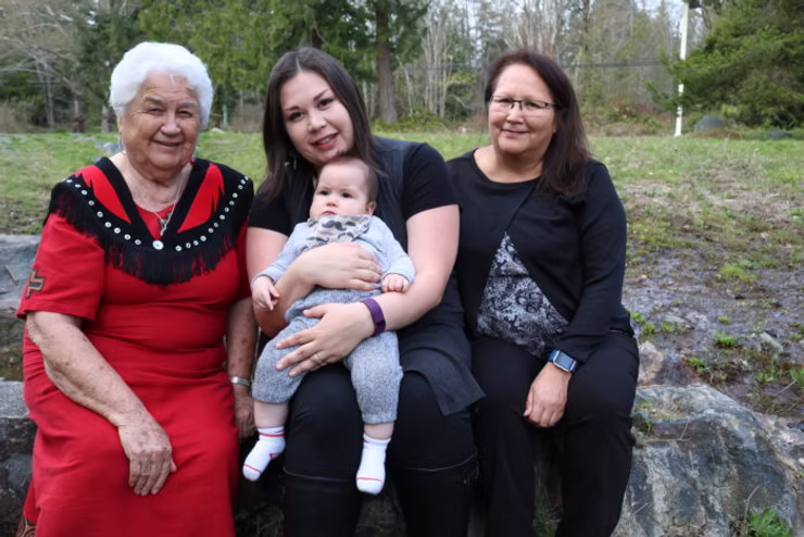 Elder Elsie Paul in a red dress beside two women and a baby sitting together outdoors